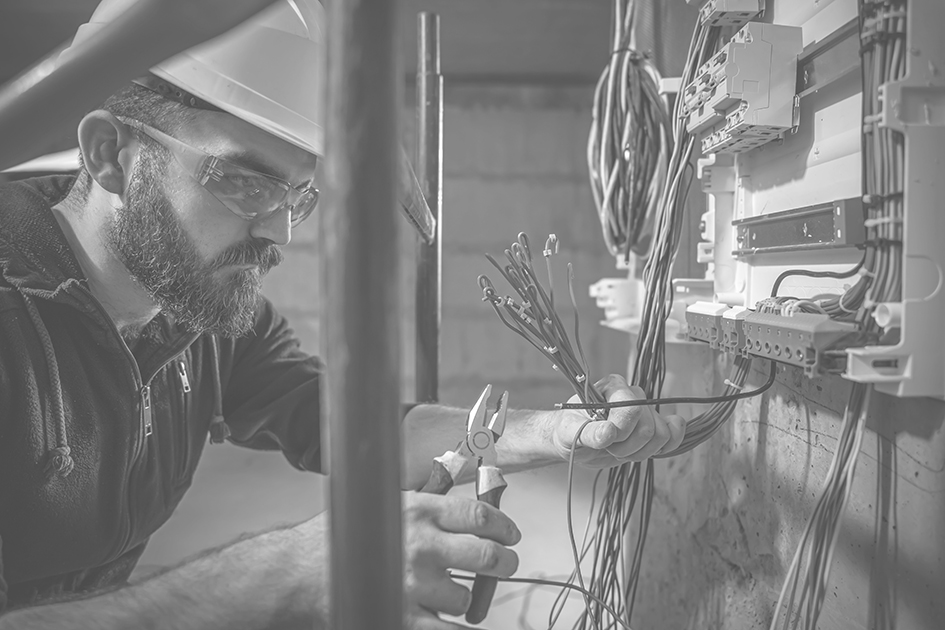 a male electrician works in a switchboard with an electrical connecting cable.